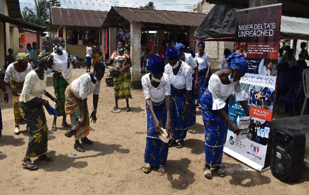 A group of women walking through a village with long skirts, in the middle of a dance, as part of a community walk through for caregivers